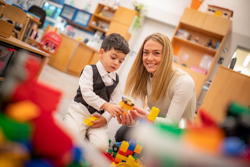 Erziehung Kind und Erzieherin spielen mit Bauklötzen.