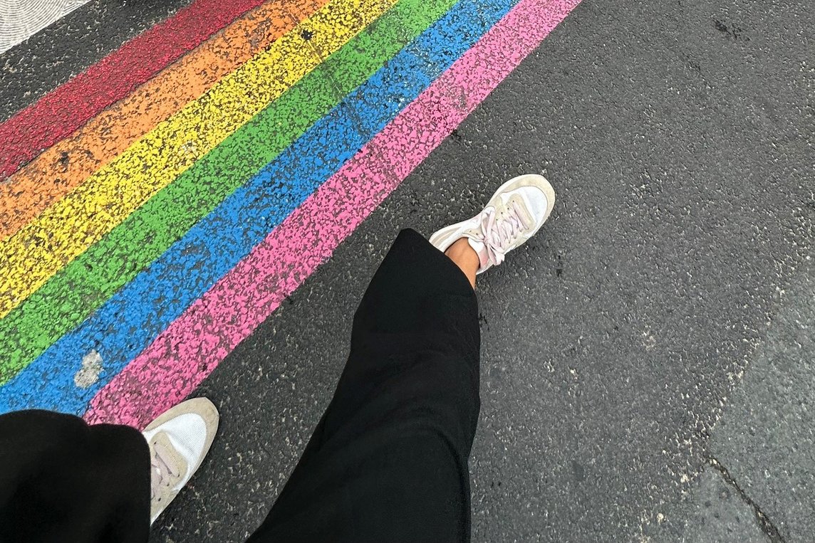 Dieses Foto zeigt die Beine einer Person, die an einem auf die Straß aufgezeichneten Regenbogen entlang läuft