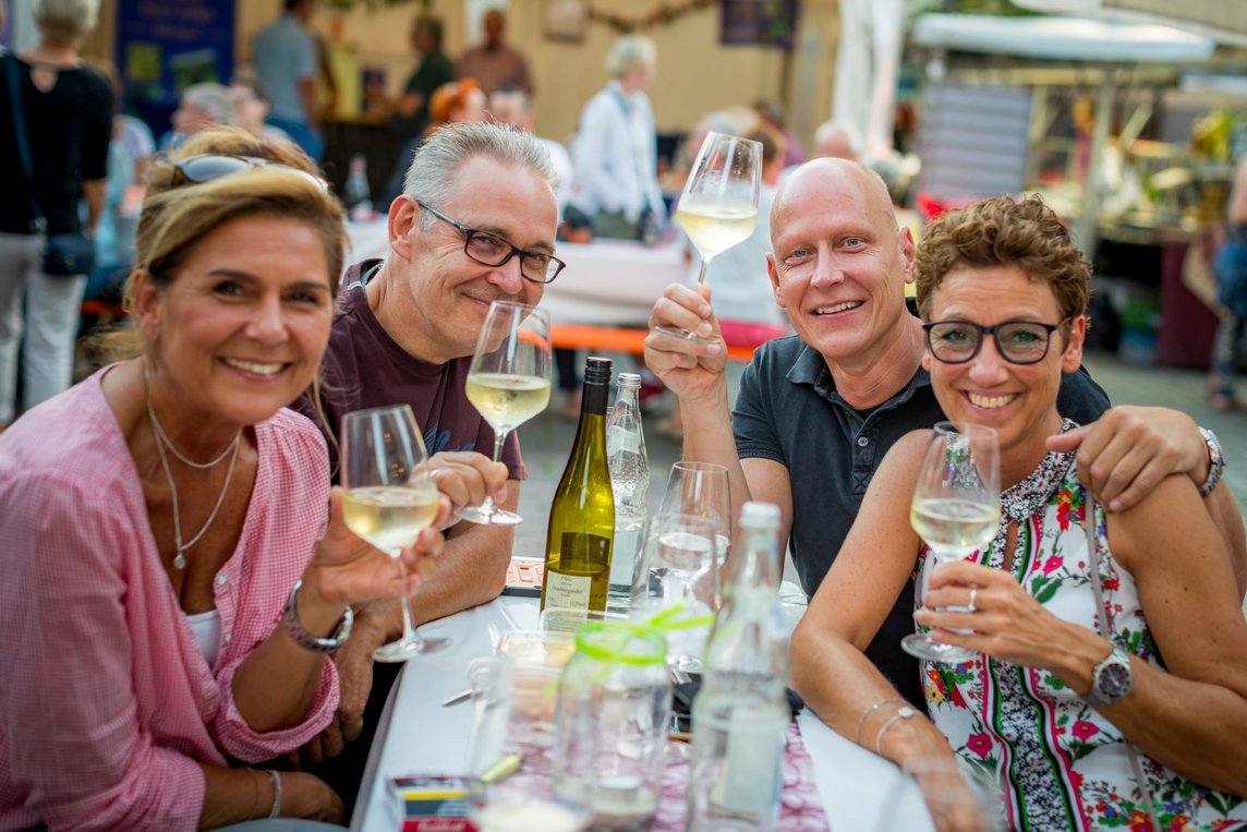 Das Bild zeigt vier gut gelaunte Menschen mit Weingläsern an einem Tisch.
