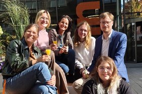 Das Foto zeigt lächelnde Menschen mit gefüllten Gläsern auf dem Markt der Möglichkeiten.