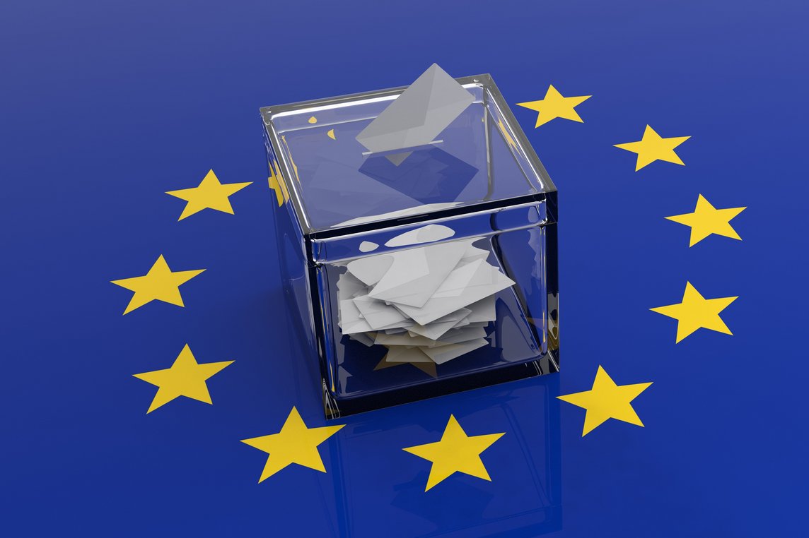 Das Foto zeigt eine durchsichtige Wahlurne auf einer Europa-Flagge.