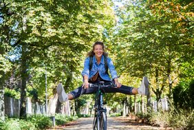 Das Bild zeigt eine fröhliche Frau mit seitlich ausgestreckten Beinen auf einem Fahrrad.