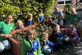 Das Foto zeigt die Kinder und Erwachsenen, die rund um das bepflanzte Hochbeet hocken.