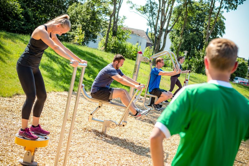 Das Bild zeigt junge Leute, die an Sportgeräten im Freien trainieren.