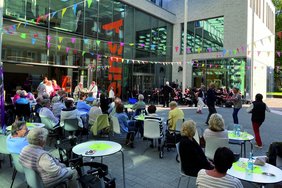 Das Bild zeigt Menschen an Bistro-Tischen, tanzende paar und ein Orchester auf dem Markt der Möglichkeiten.
