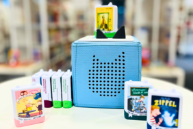 Auf dem Foto sieht man eine hellblaue Toniebox um die verschiedene Book Tonie-Figuren aufgestellt wurden.