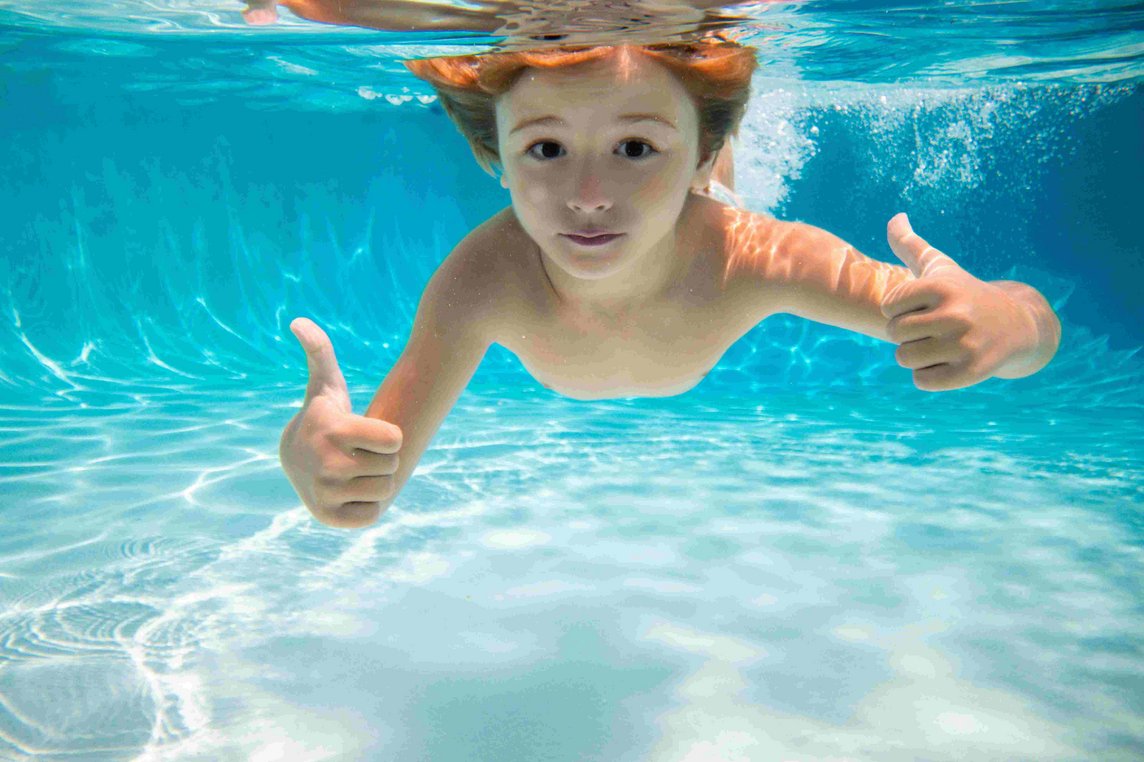 Child swims underwater in swimming pool, happy active boy dives and has fun under water, kids watersport. Children play in tropical resort. Family beach vacation and summer activity.