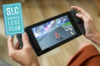 Jemand hält eine Nintendo Switch Konsole in den Händen auf der das Spiel "Mario Kart" läuft.