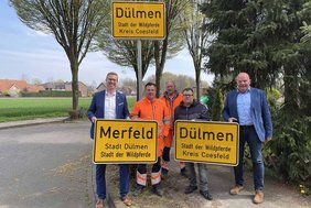 Dieses Foto zeigt Bürgermeister Carsten Hövekamp und städtische Mitarbeitende beim Aufhängen des neuen Ortsschildes "Stadt der Wildpferde". 