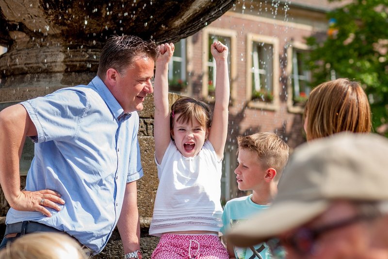 Familie sitzt vor einem Brunnen. Kind lacht.