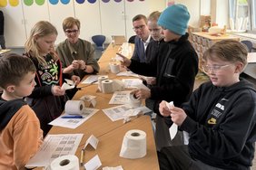 Das Bild zeigt die Personen, während sie verschiedenen Toilettenpapierrollen untersuchen.