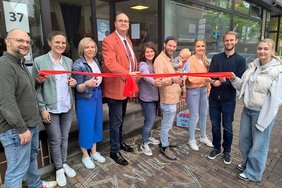 Ankerpunkt rotes Band Das Foto zeigt Sozialdezernent Christoph Noelke, der gemeinsam mit Mitarbeitenden des Fachbereichs Jugend und Familie das rote Band durchschneidet.