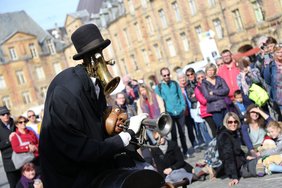 Das Bild zeigt eine Figur vor großem Publikum auf einem Platz.