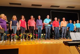 Das Bild zeigt die Sängerinnen und Sänger in farbenfrohen Oberteilen.