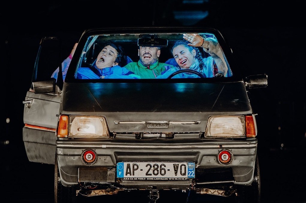 Das Foto zeigt die drei Darsteller des Société Protectrice de Petites Idées, die in einem Auto sitzen und vom Licht geblendet werden