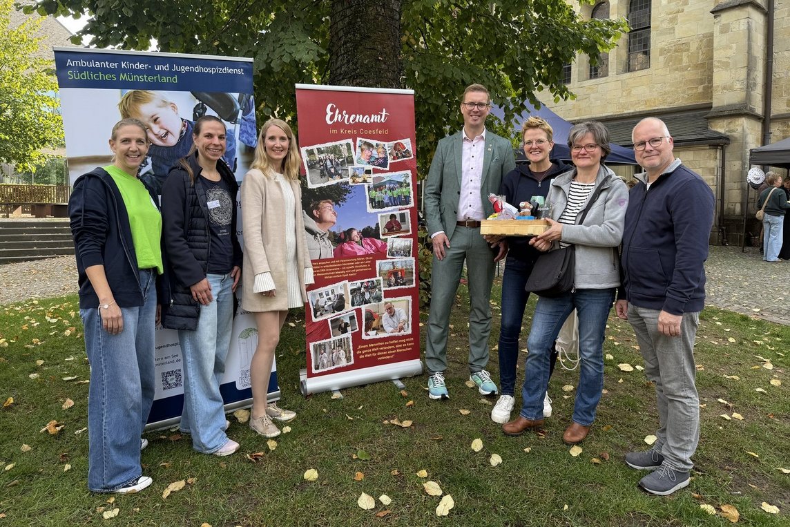 Bürgermeister Carsten Hövekamp (Mitte) übergab einen Präsentkorb an Hilla Berheide vom AKHD (3. v. re.) sowie Leonie und Andreas Steens. Zur Prämierung des bewegenden Fotos, das groß auf dem Banner zu sehen ist, gratulierten die Ehrenamtskoordinatorinnen Verena Rohlmann (2. v. li.) aus Dülmen und Vanessa Kalkhoff (3. v. li.) aus Nottuln sowie Yvonne Steinbuß, hauptamtliche Koordinatorin vom AKHD Südliches Münsterland. Foto: Stadt Dülmen/Kannacher
