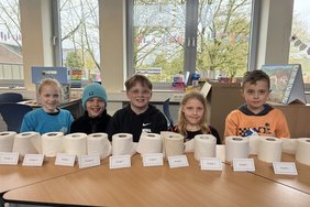 Das Foto zeigt die Schülerinnen hinter eine Reihe von Toilettenpapierrollen.