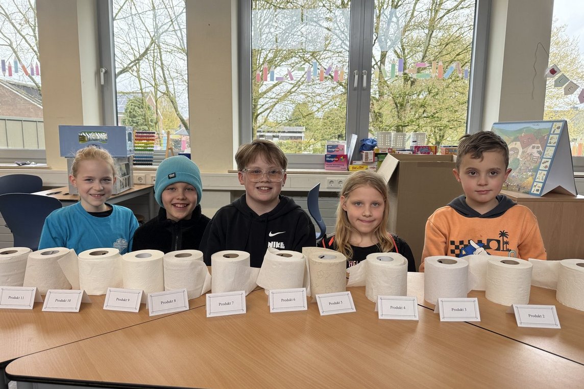 Das Foto zeigt die Schülerinnen hinter eine Reihe von Toilettenpapierrollen.