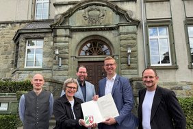 Vor der Hermann-Leeser-Schule: Kirsten Apke-Lobmeyer vom städtischen Fachbereich Bauaufsicht und Denkmalschutz überreicht im Namen des Landes NRW die Denkmalplakette nebst Urkunde an Bürgermeister Carsten Hövekamp. Auch Stadtbaurat Markus Mönter (Mitte), Stadtarchivar Dr. Stefan Sudmann (li.) und Robert Schneider, Leiter der Hermann-Leeser-Schule, freuen sich über die Auszeichnung. Foto: Stadt Dülmen/Kannacher