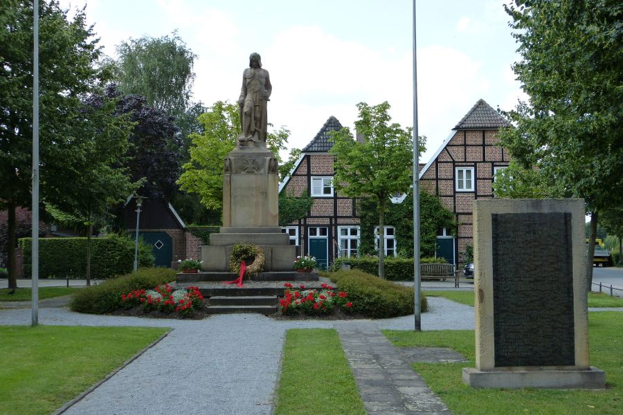 Das Bild zeigt den Dorfplatz im Hiddingsel mit Fachwerkhäusern und Denkmal.